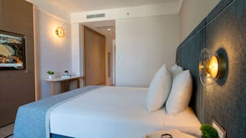 Una habitación de hotel moderna con una cama grande, lámparas de noche, una mesita con un libro y una planta, y un cuadro en la pared.