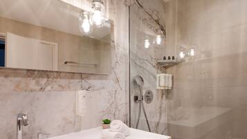 A modern bathroom with a marble wall, a white sink, a glass shower enclosure, and a small potted plant.