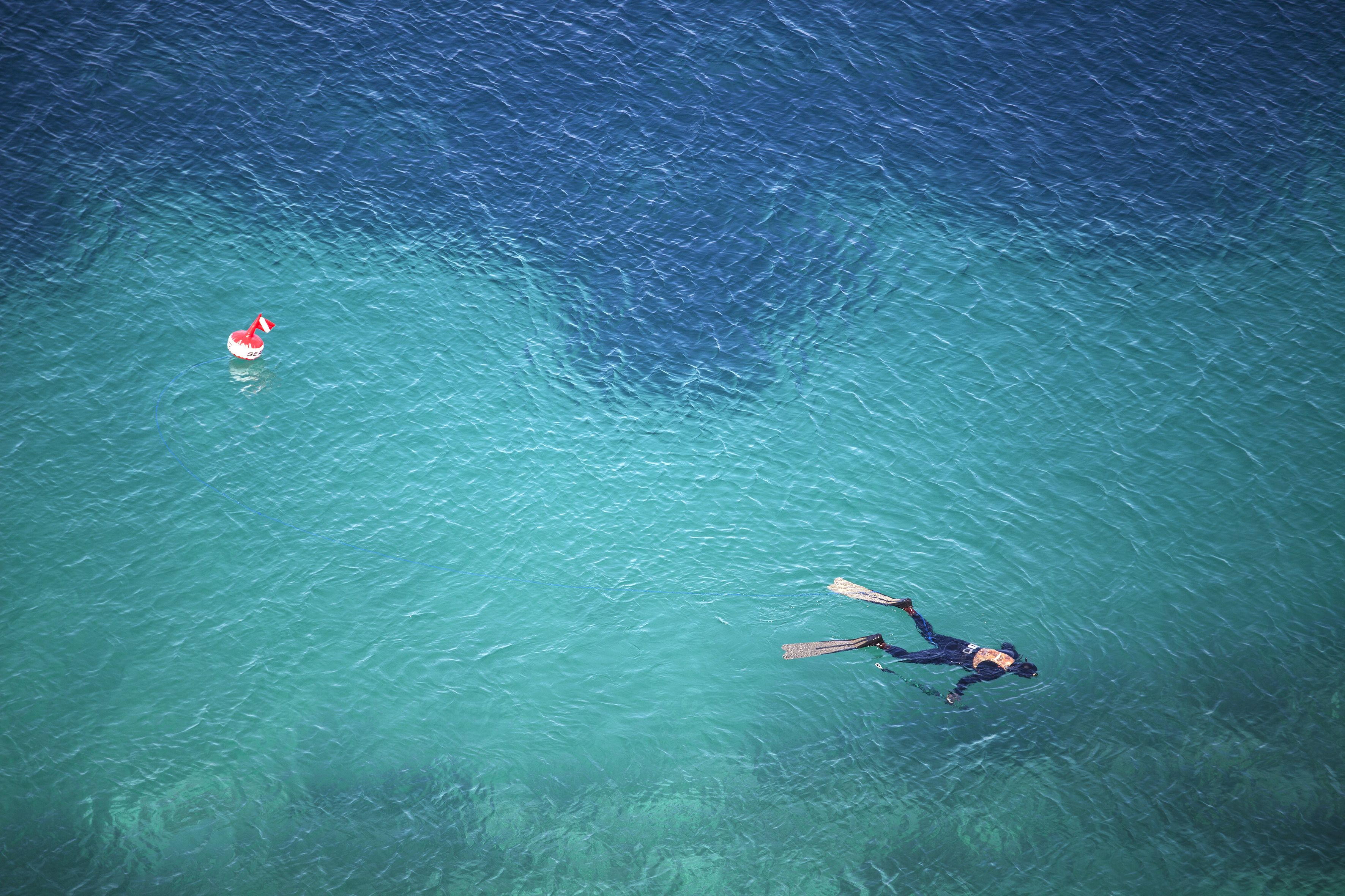 An aerial view of a person swimming in clear blue water with a red and white object nearby.