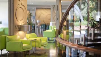 A modern hotel lobby with green seating, a glass railing, and a central light fixture.