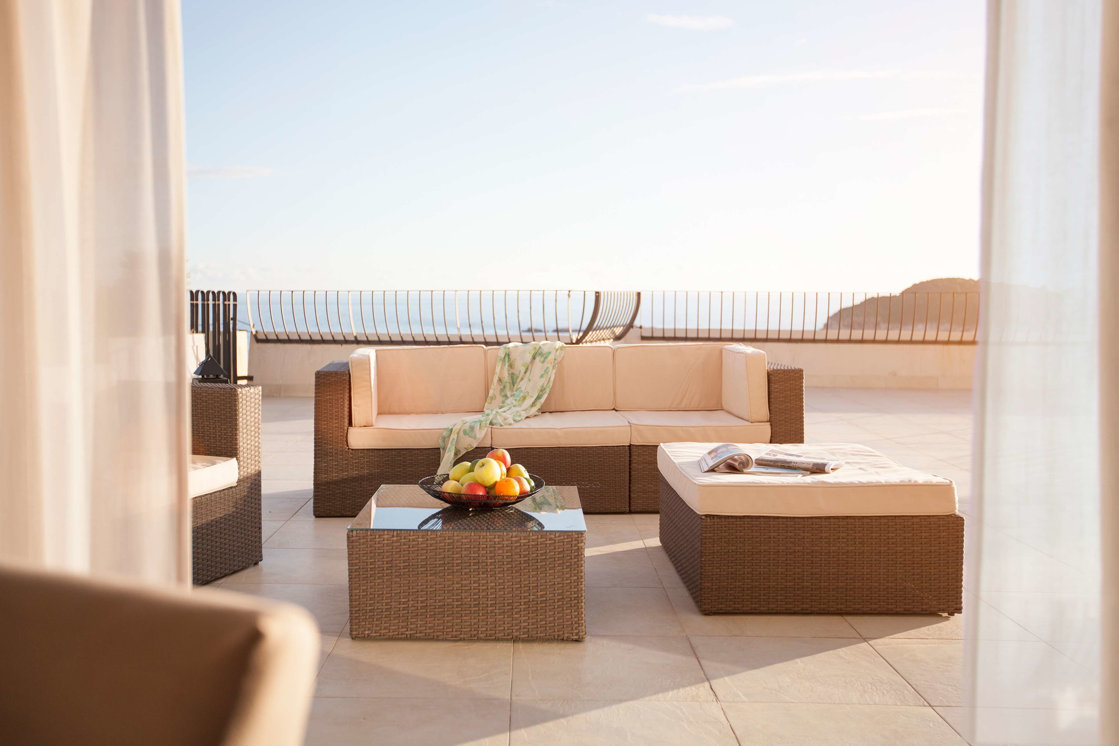 A rooftop lounge area with wicker furniture, a sofa, and a coffee table with fruit.