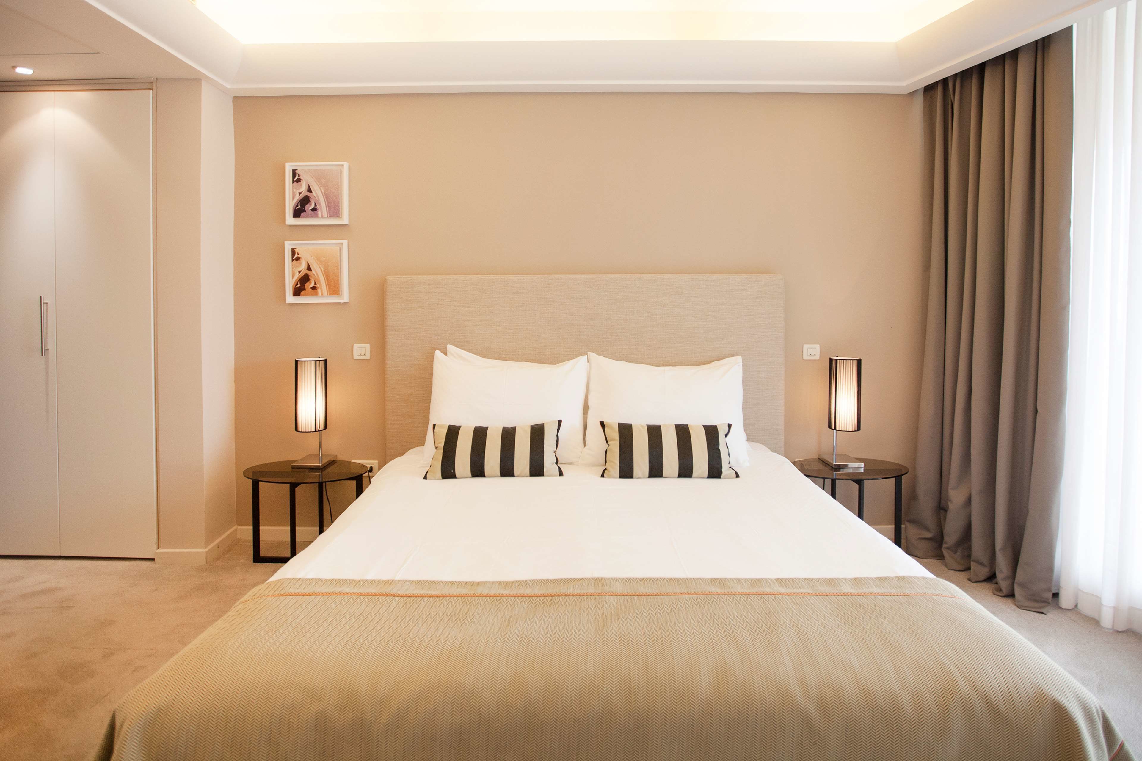 Habitación de hotel con una cama grande, dos mesitas de noche con lámparas, un armario y dos cuadros en la pared.