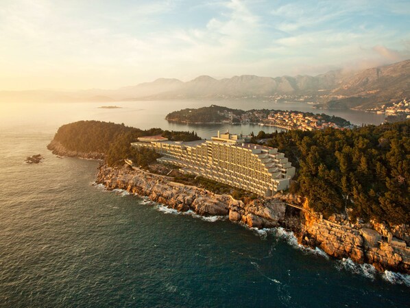 A coastal hotel with multiple buildings, a rocky shoreline, and a view of the sea and distant mountains. - Hotel Croatia (Konavle)
