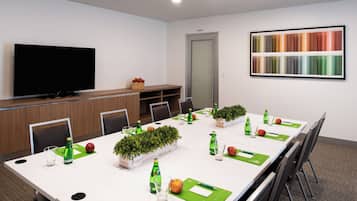 Uma sala de conferências com uma mesa comprida, cadeiras, uma televisão e uma paleta de cores na parede.