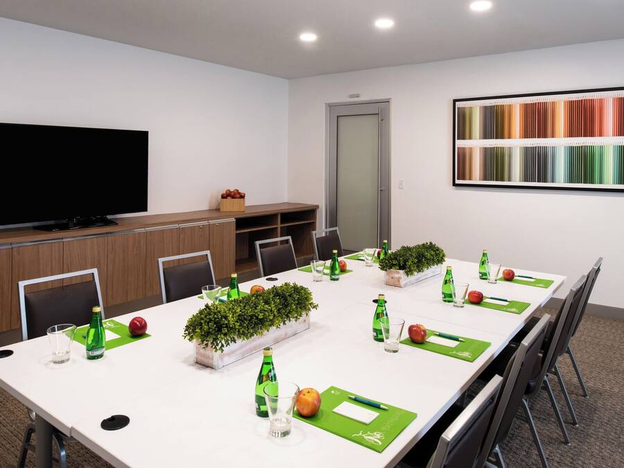 Uma sala de conferências com uma mesa comprida, cadeiras, uma televisão e uma paleta de cores na parede.