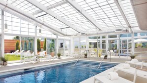 Une piscine intérieure aux parois en verre transparent, dotée de chaises longues blanches et présentant un design architectural moderne.