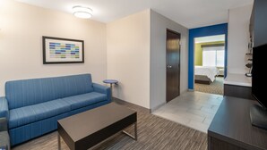A hotel room with a blue sofa, a small table, a framed picture on the wall, a door leading to a bathroom, and a TV on a stand. - Holiday Inn Express & Suites Trinidad by IHG (Trinidad)