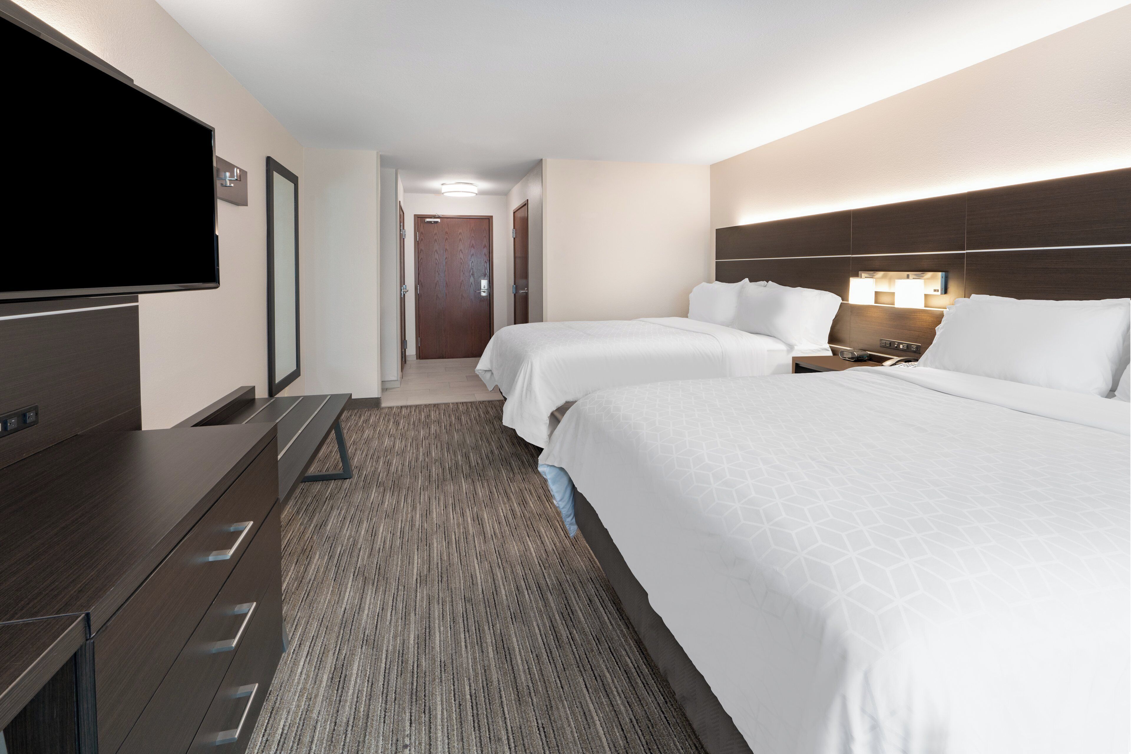 Habitación de hotel con una cama grande, televisión, escritorio y puerta que conduce a otra habitación.