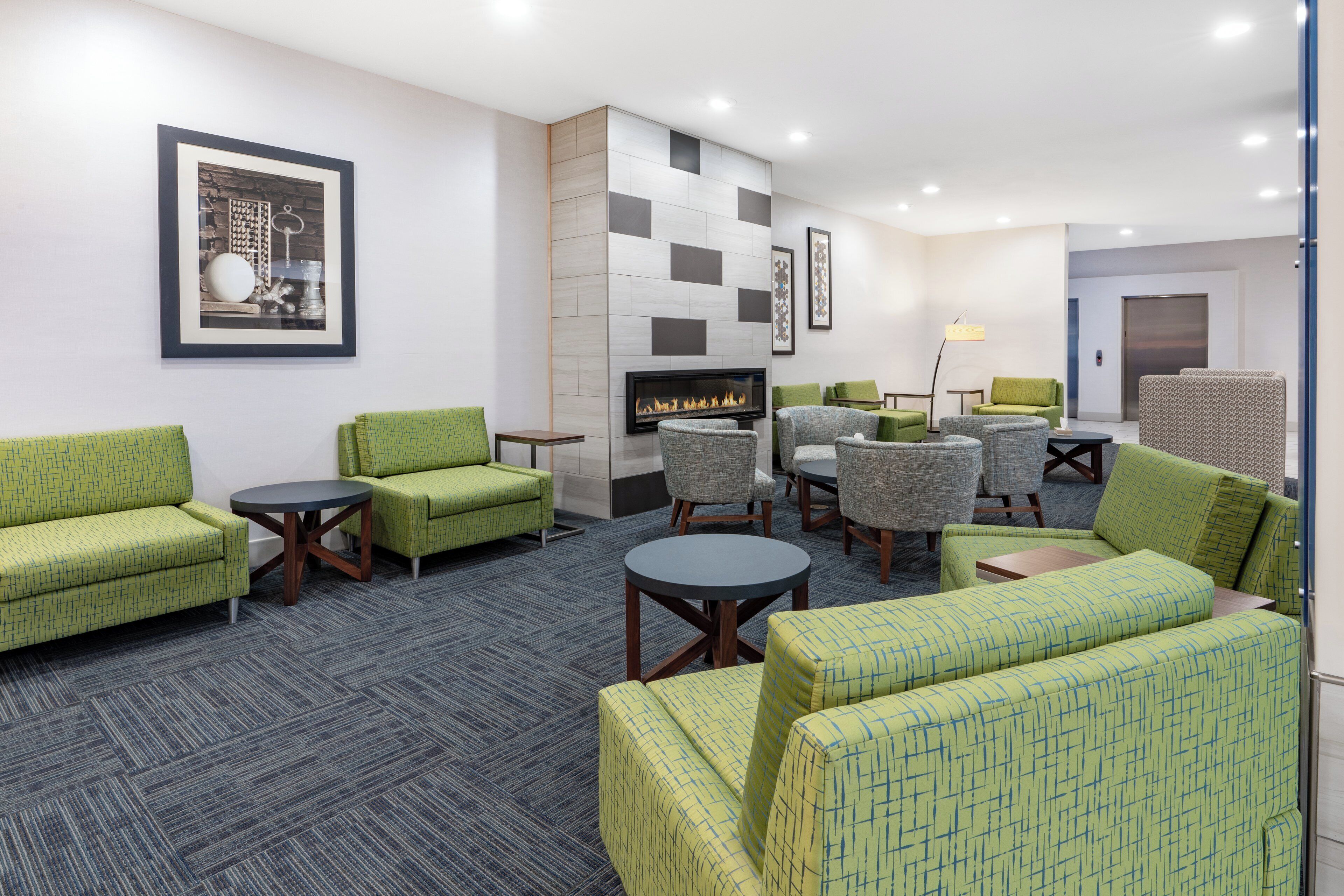 A hotel lobby with green upholstered sofas, a fireplace, and a modern tiled wall.