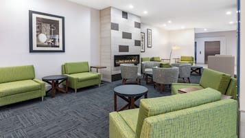 A hotel lobby with green upholstered sofas, a fireplace, and a modern tiled wall.