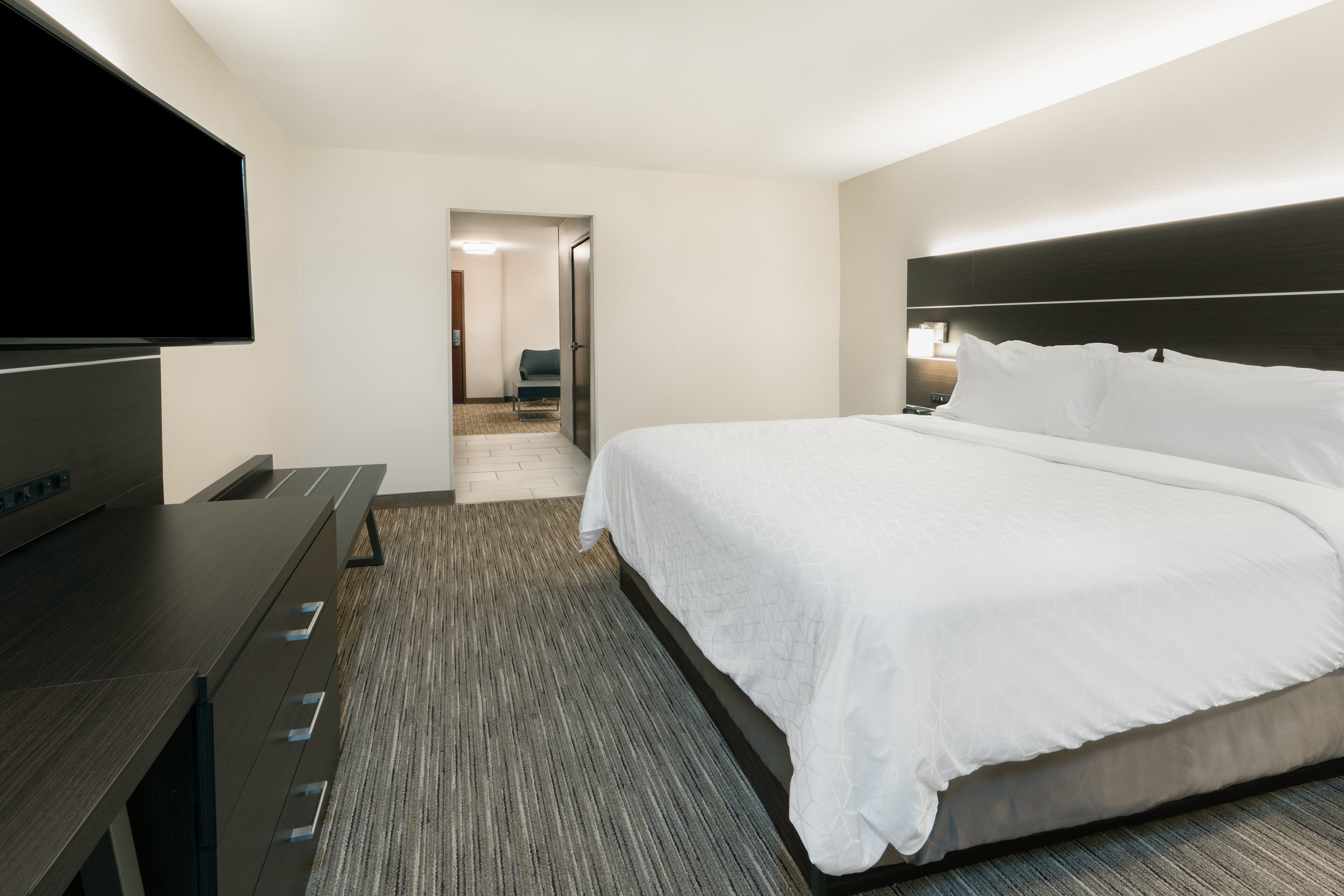 A hotel room with a large bed, a flat-screen TV, a desk, and a carpeted floor.