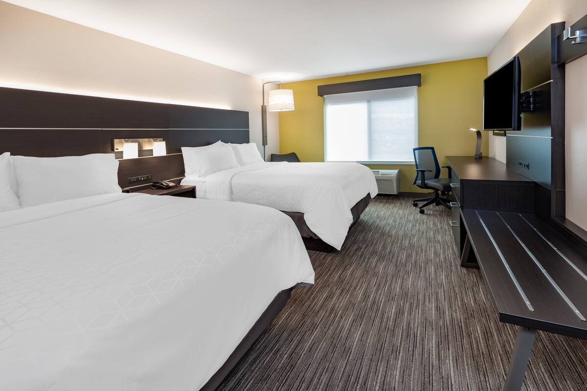A hotel room with two beds, a desk, a chair, a TV, and a window.