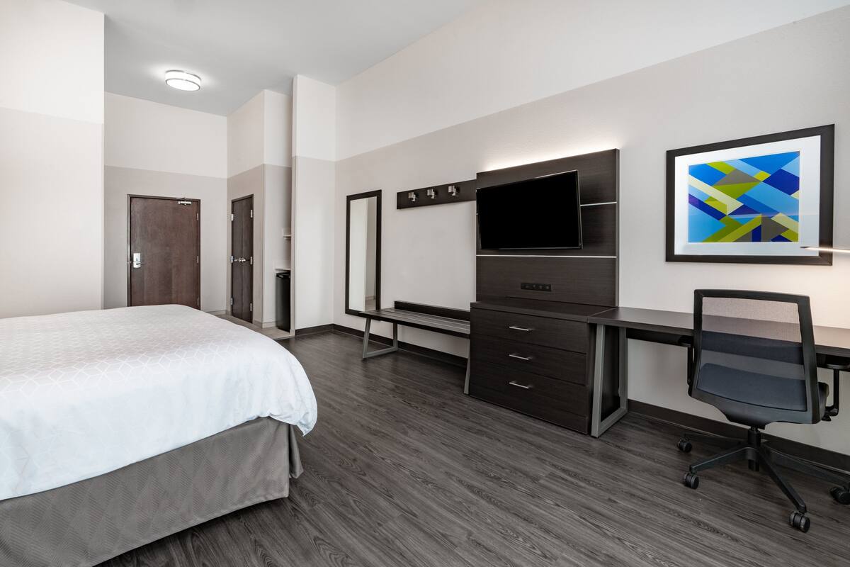 A hotel room with a bed, a desk, a chair, a TV, and a framed picture on the wall.