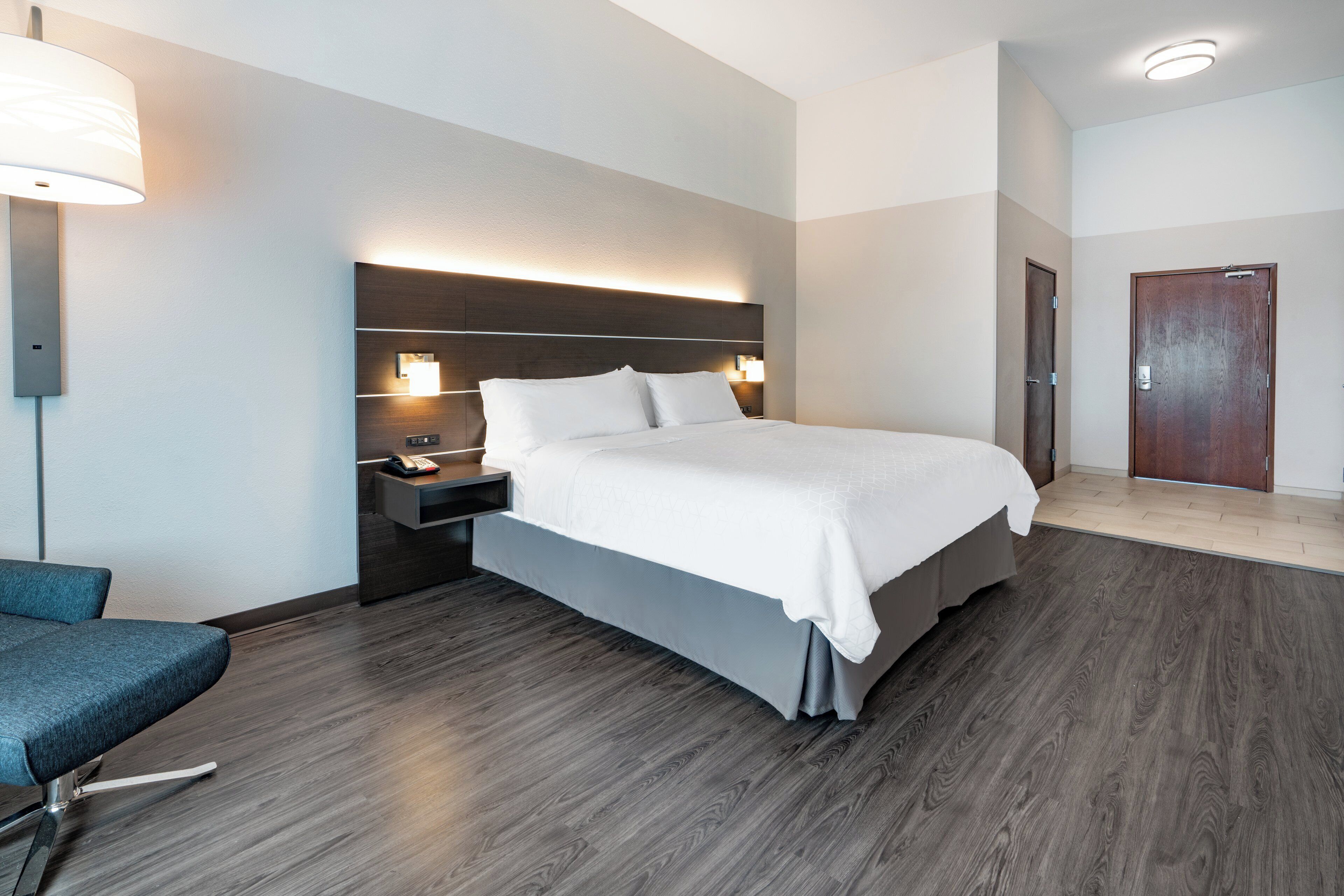 A hotel room with a large bed, bedside tables, a desk, a chair, and a door.