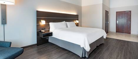 A hotel room with a large bed, bedside tables, a desk, a chair, and a door.