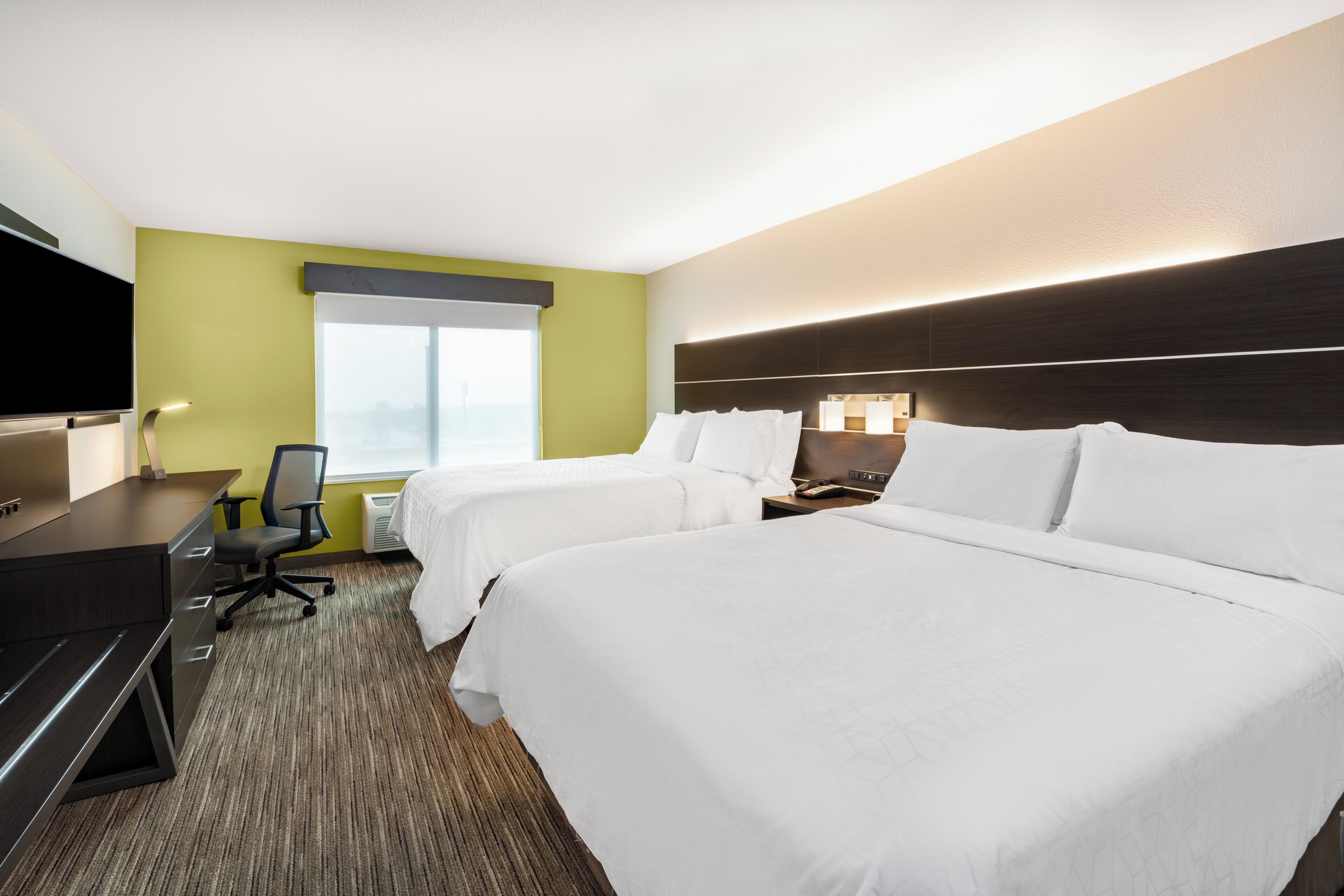 A hotel room with two beds, a desk, a chair, a television, and a window.