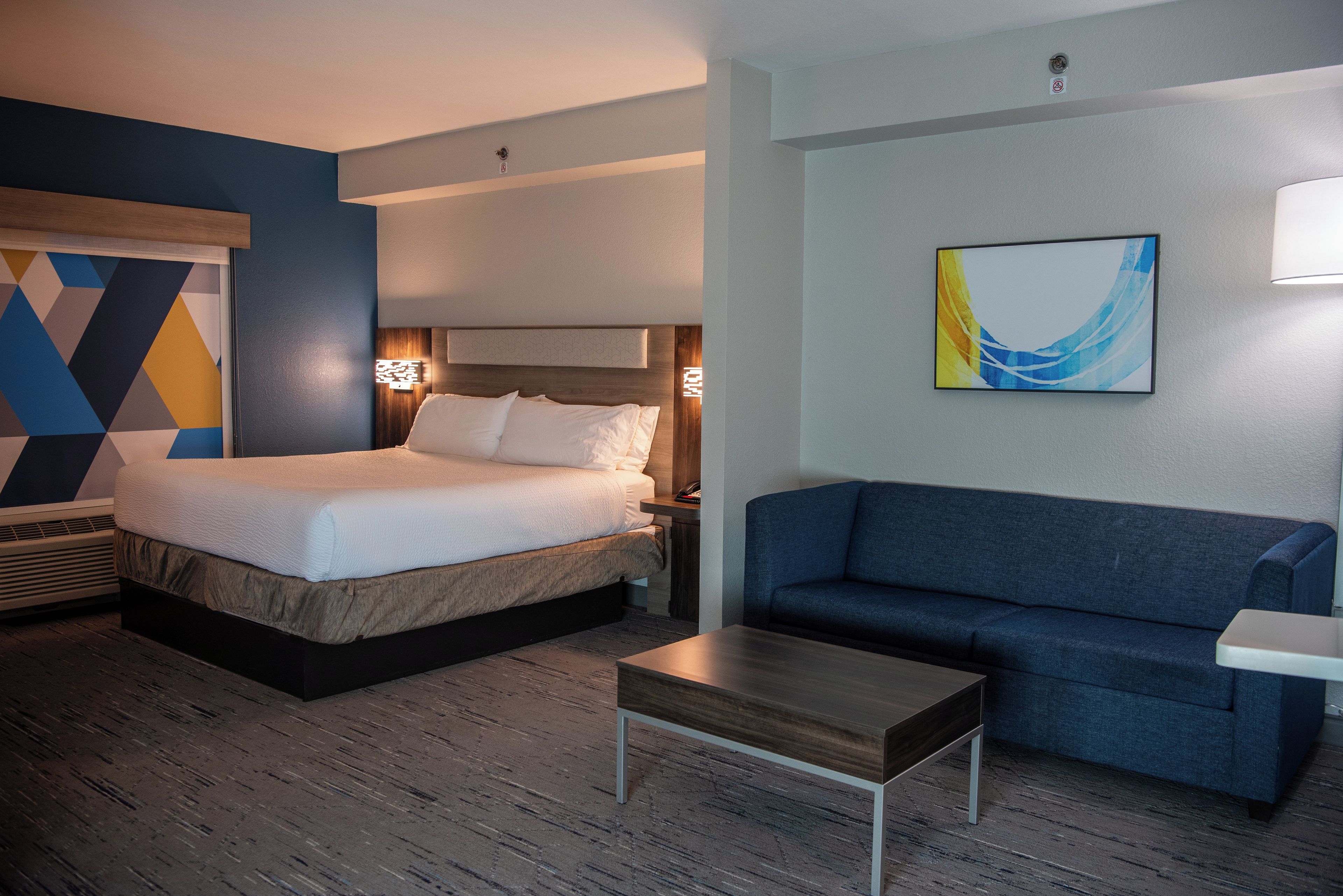 A hotel room with a bed, a sofa, a small table, and a wall-mounted painting.