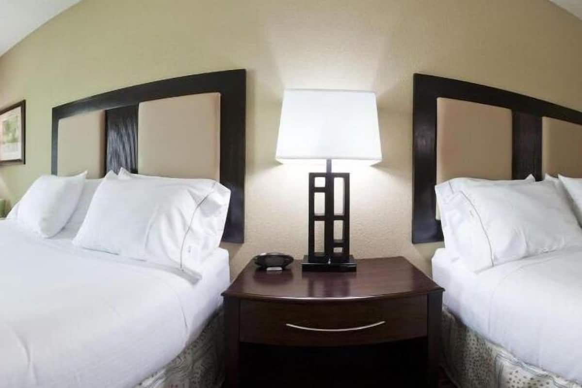 Een hotelkamer met twee bedden, een nachtkastje met een lamp en een lijst aan de muur.