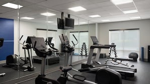 Ein Fitnessstudio mit verschiedenen Trainingsgeräten, darunter Laufbänder, ein Crosstrainer und Kurzhanteln.