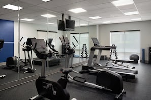 Une salle de sport équipée de divers appareils d’exercice, notamment des tapis de course, un vélo elliptique et des poids libres.