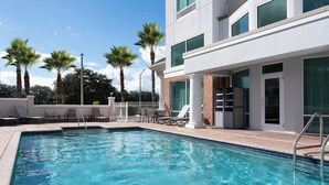 Ein Pool mit Fliesen, Palmen und ein modernes Gebäude mit großen Fenstern und einer Ziegelaußenwand.