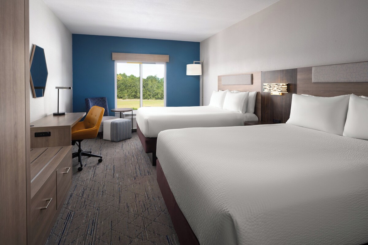 Habitación de hotel con dos camas, un escritorio, una silla y vistas al exterior.