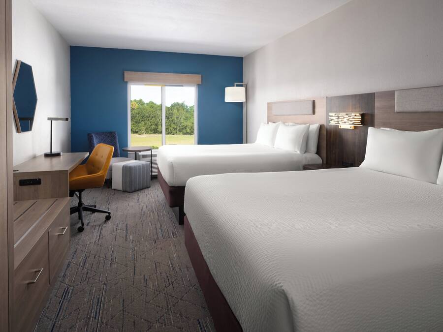 A hotel room with two beds, a desk, a chair, and a view of the outdoors.