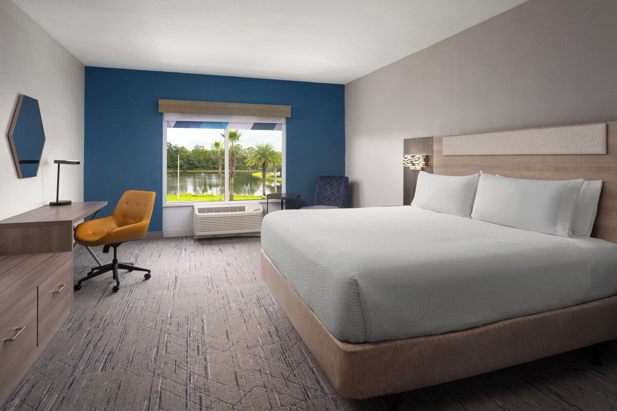 Een hotelkamer met een groot bed, een bureau met stoel, een raam met uitzicht op een meer en een wandlamp.