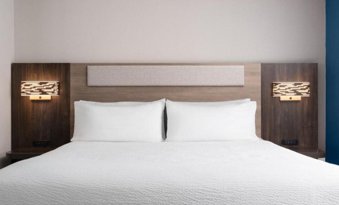 Una habitación de hotel con una cama grande, dos mesitas de noche e iluminación en la pared.