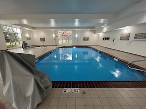 An indoor swimming pool with a covered area, tiled flooring, and safety signs on the walls.