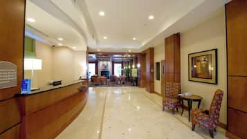 A hotel lobby with a reception desk, seating area, and a hallway leading to meeting rooms.