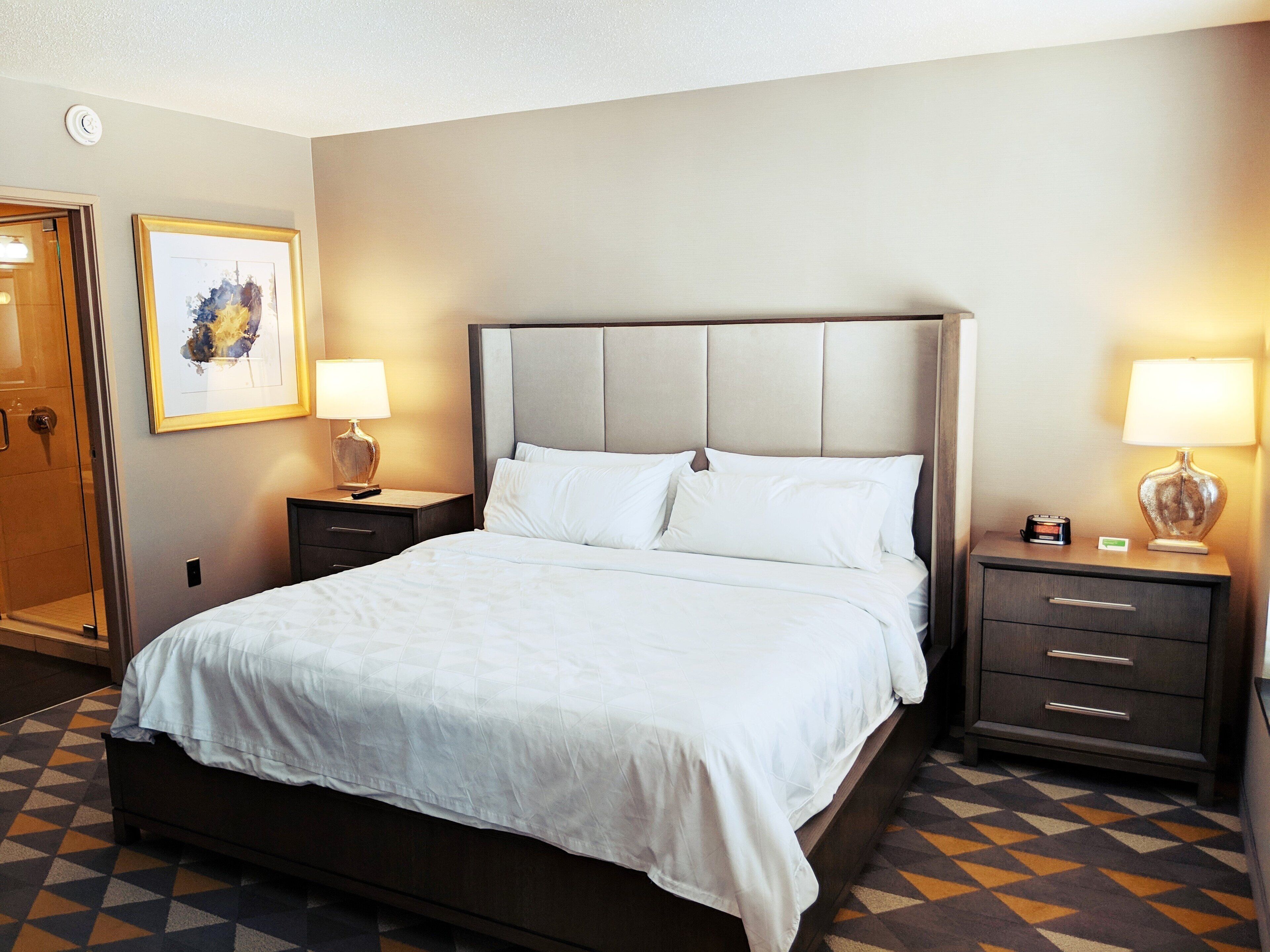 A hotel room with a large bed, two bedside tables with lamps, a framed picture on the wall, and a patterned floor.