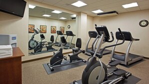 A gym with multiple exercise machines, a mirror, and a clock on the wall.