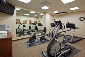 A gym with multiple exercise machines, a mirror, and a clock on the wall.
