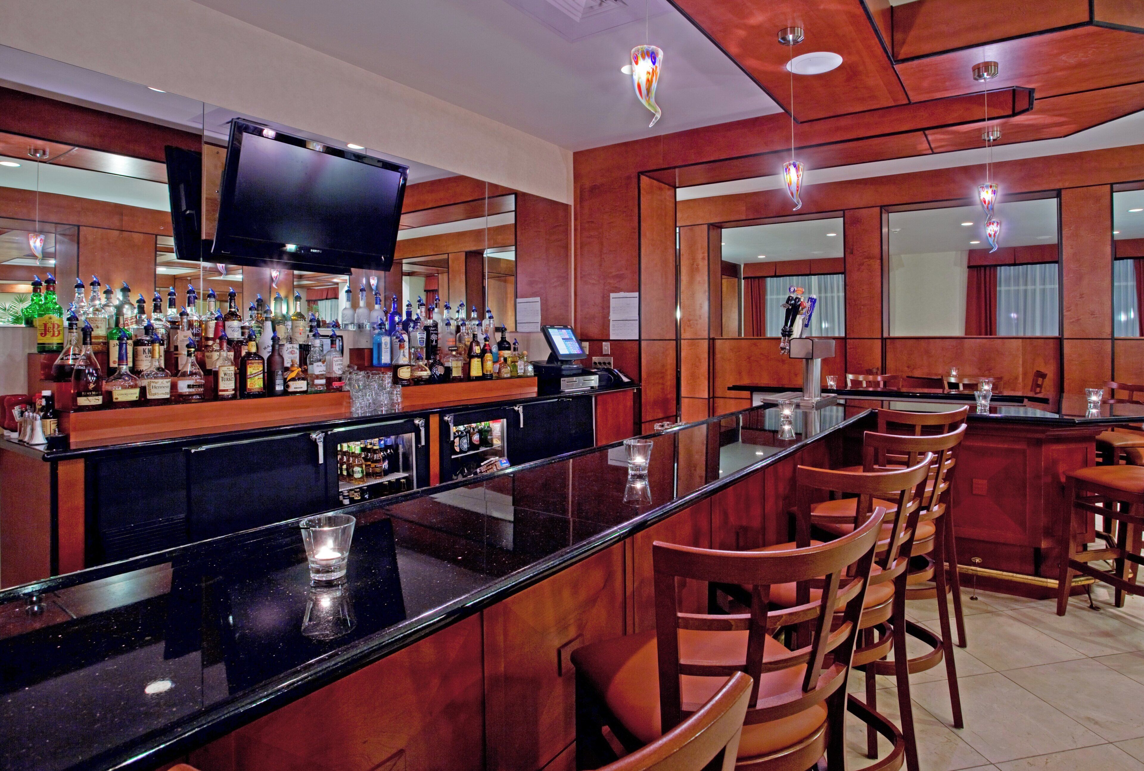 A bar area with a long counter, multiple seating options, and a television mounted above the bar.