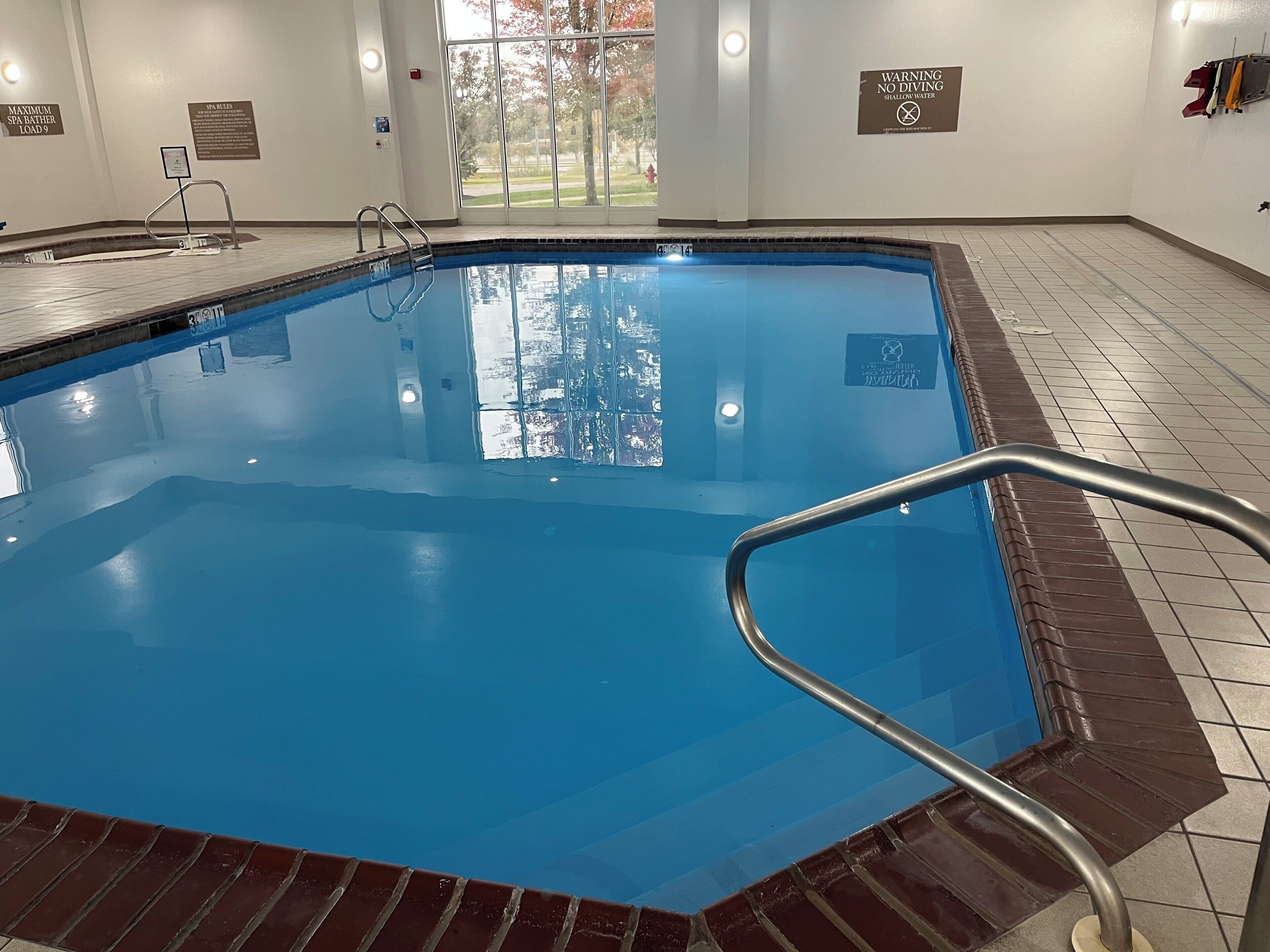 Una piscina interior con agua cristalina, una escalera de metal y suelo de baldosas.