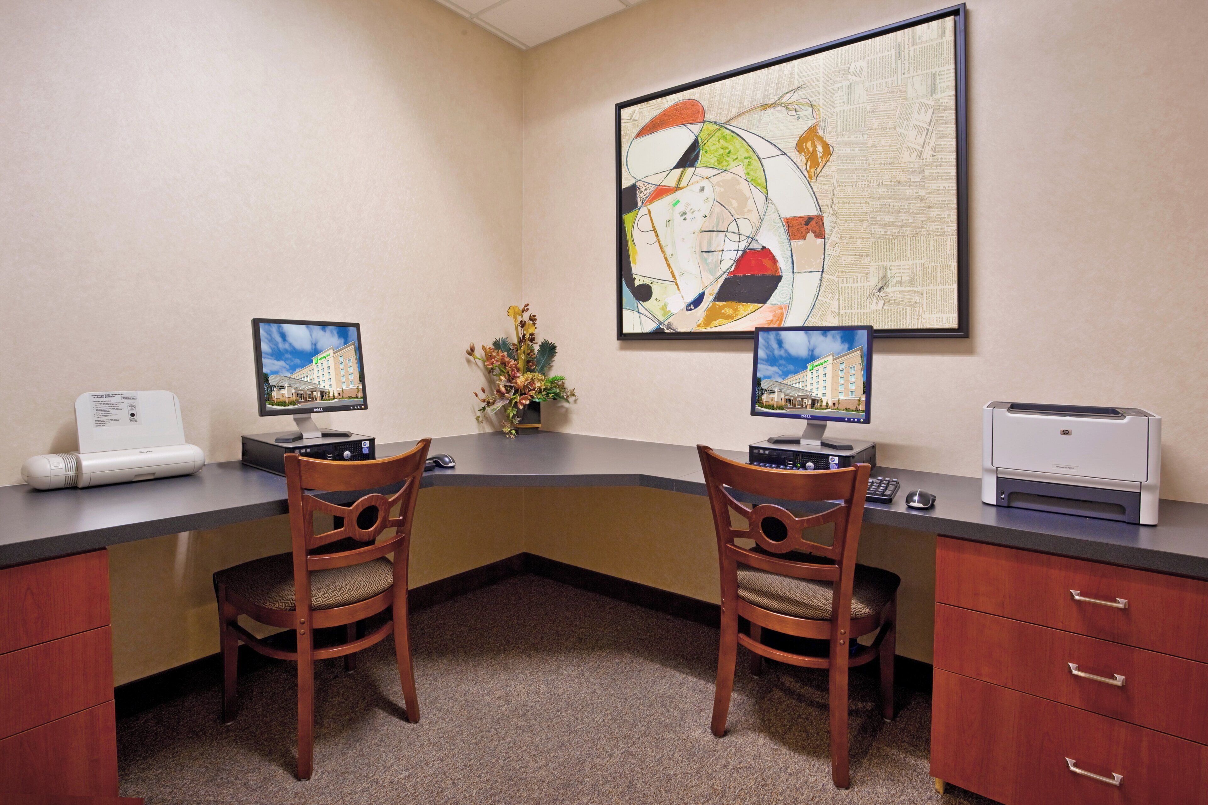A hotel office with two desks, two chairs, a printer, and a large abstract painting on the wall.