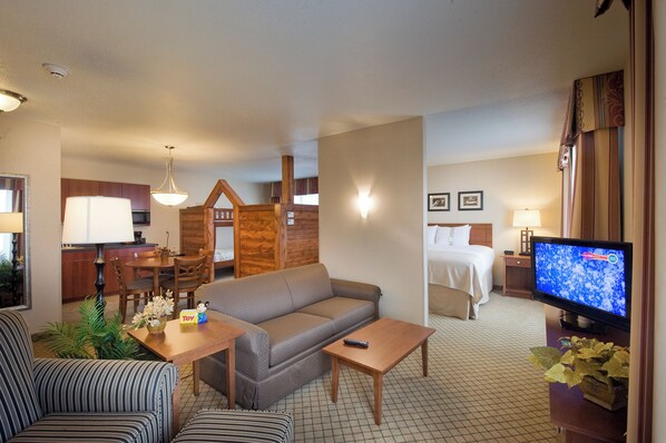 A hotel room with a sofa, a dining table, a TV, and a bed. - Holiday Inn Purdue - Fort Wayne by IHG (Fort Wayne)