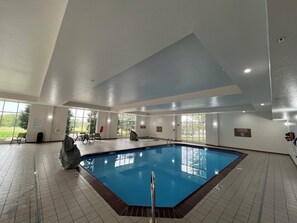 A large indoor swimming pool with clear views of the outdoors through large windows, a covered area, and a lifeguard stand. - Holiday Inn Purdue - Fort Wayne by IHG (Fort Wayne)