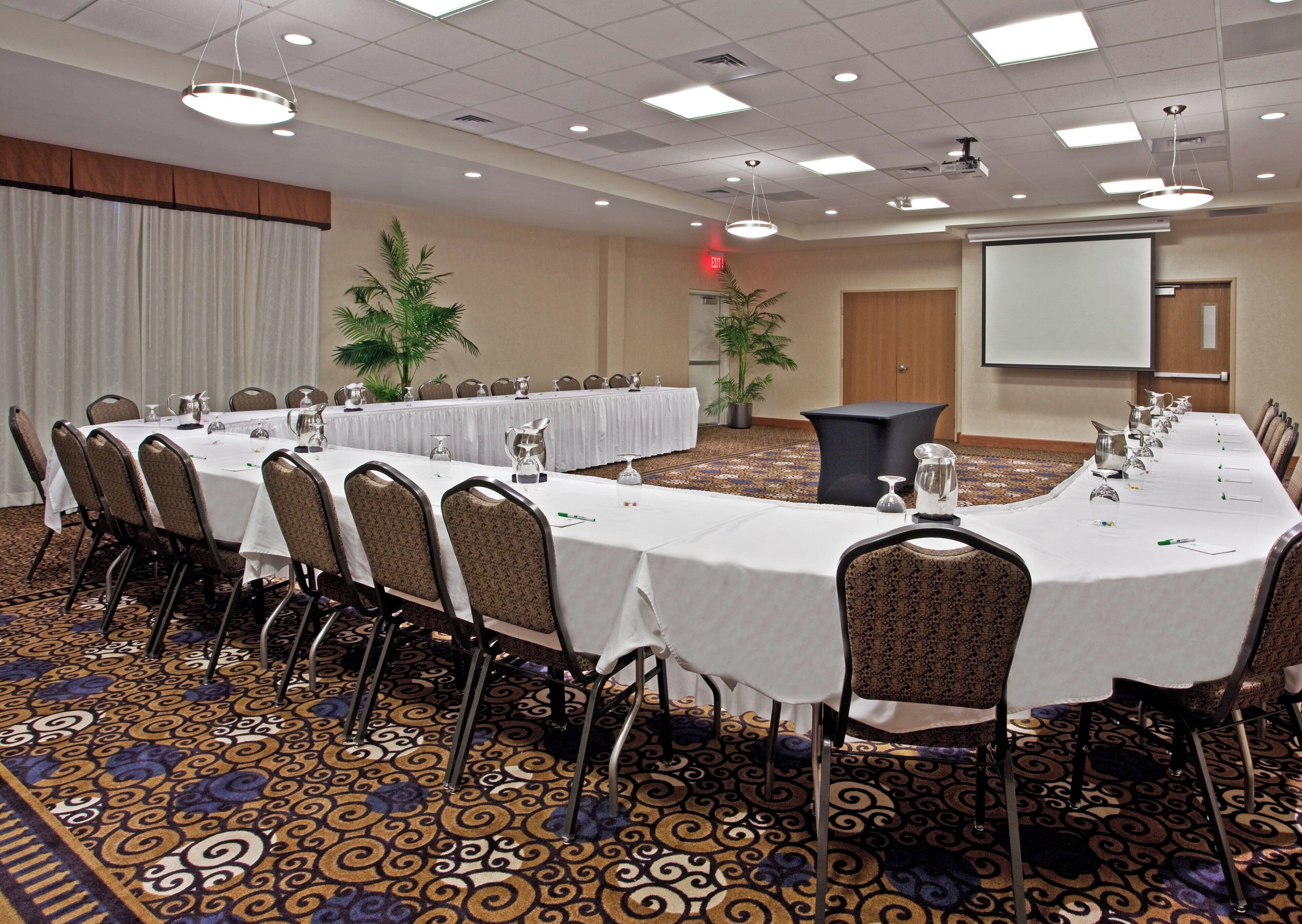 A conference room with multiple tables, chairs, and a projector screen.