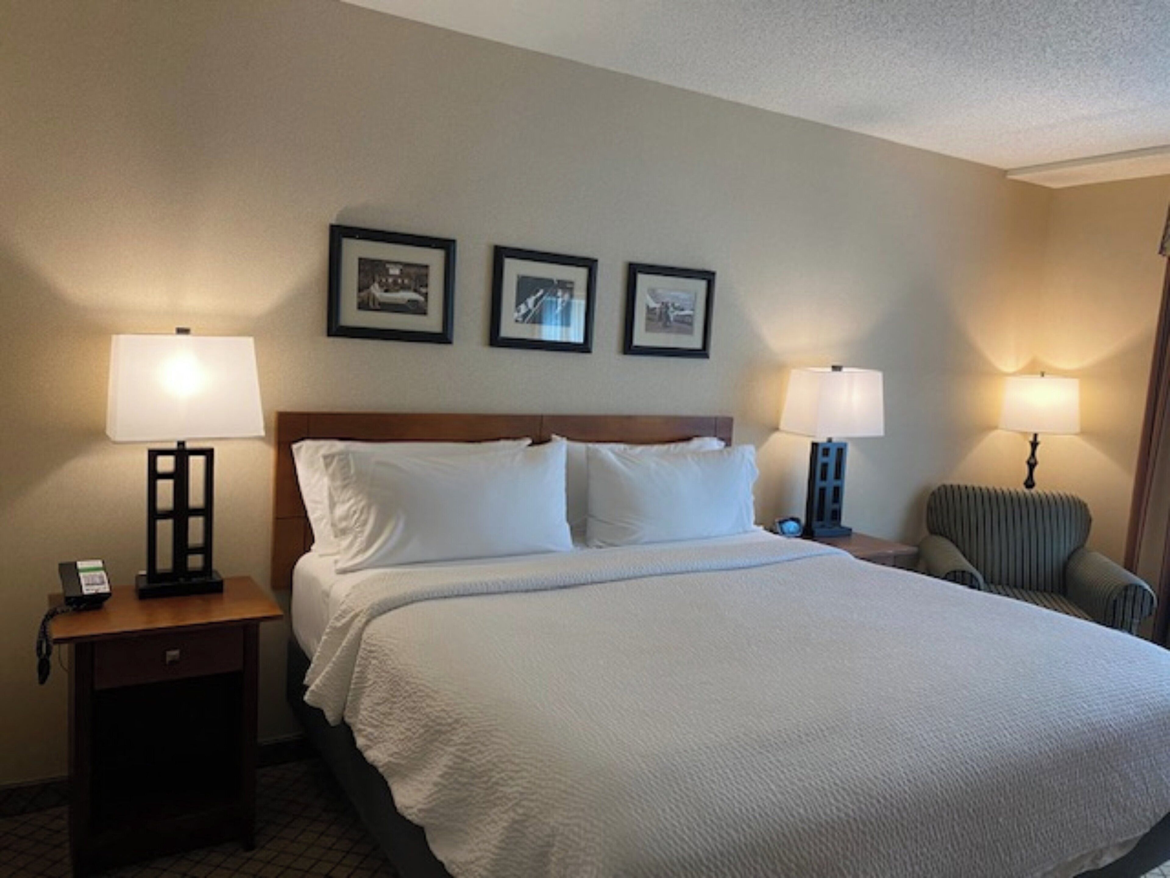 A hotel room with a large bed, two bedside tables, two lamps, and three framed pictures on the wall.