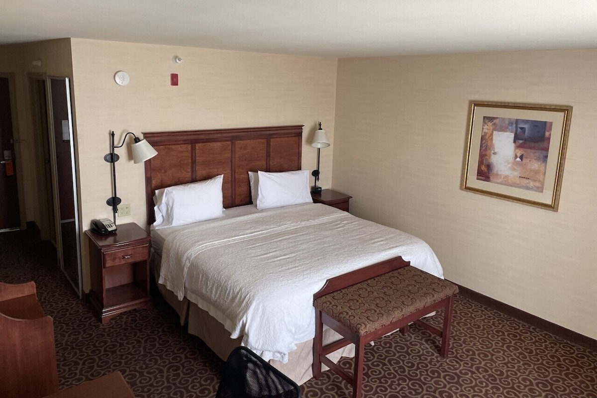 A hotel room with a large bed, bedside tables, a desk, and a chair.