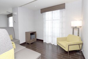 A hotel room with a sofa, a chair, a small cabinet, and a window with curtains.