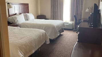 Habitación de hotel con dos camas, un escritorio, una silla y un ventanal con cortinas.