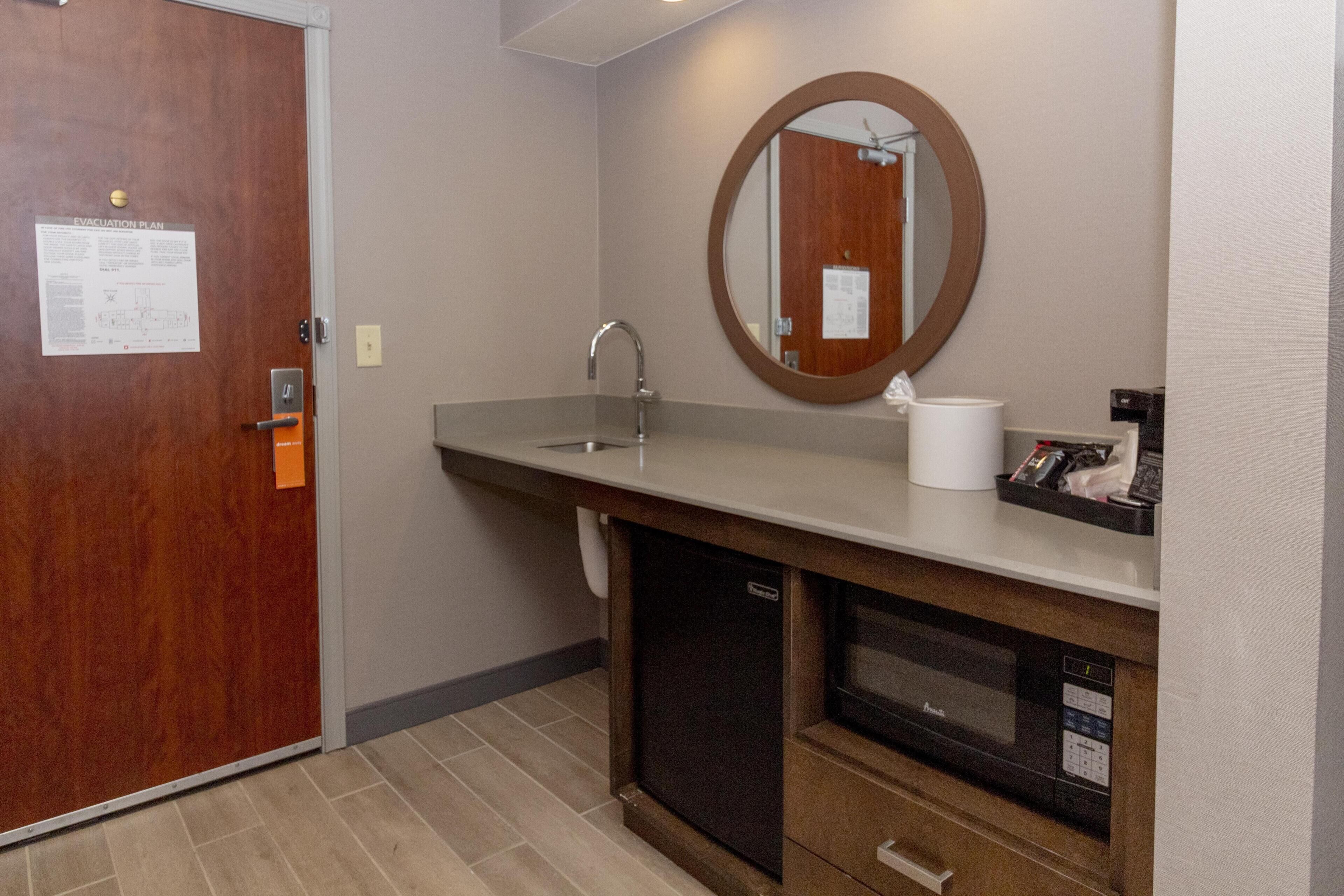 A bathroom with a wooden door, a sink, a mirror, and a towel dispenser.
