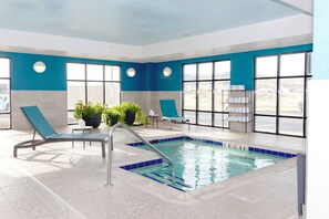 An indoor swimming pool with blue and white walls, large windows, and lounge chairs.