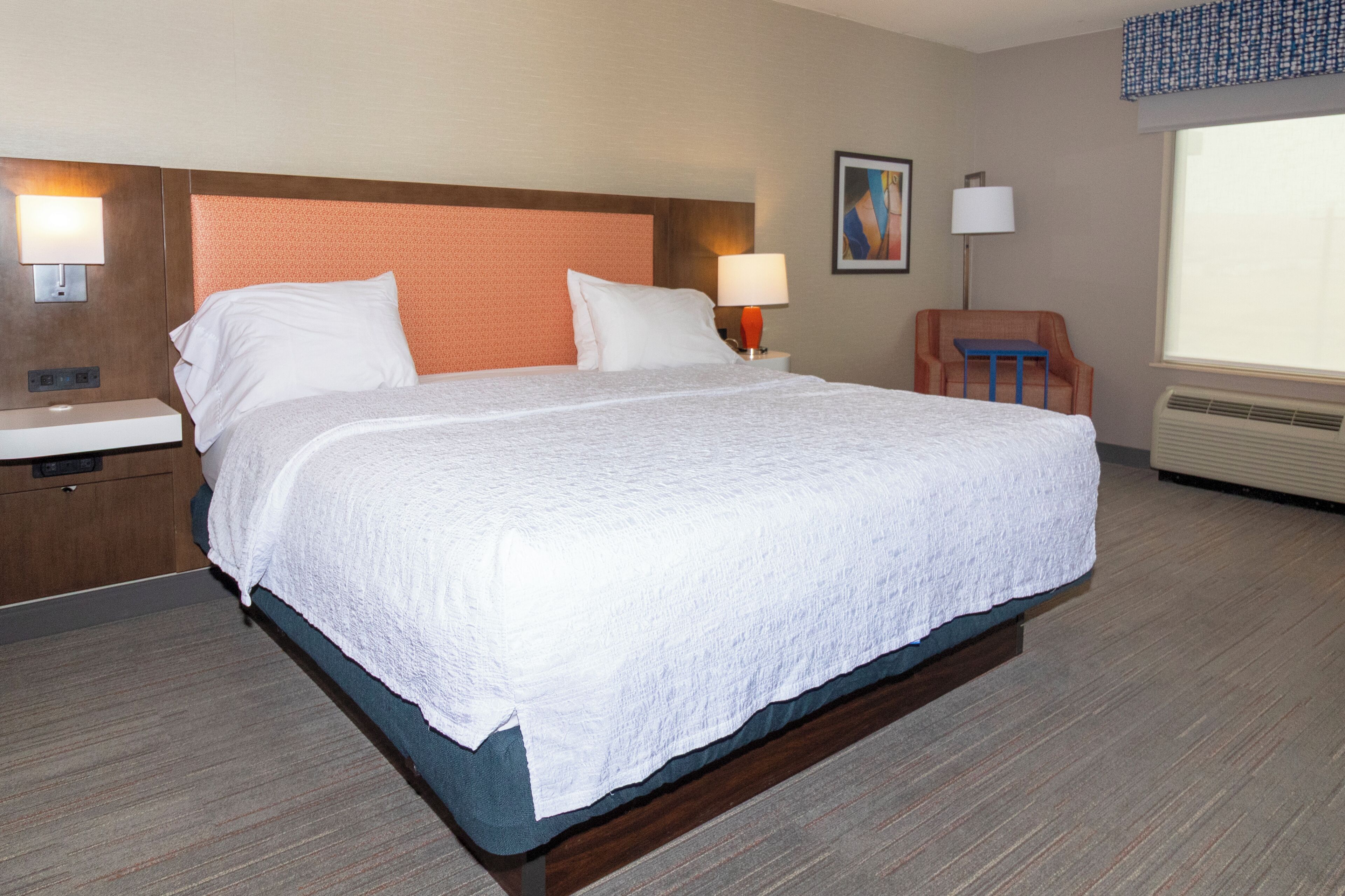 A hotel room with a large bed, a nightstand, a chair, and a window.