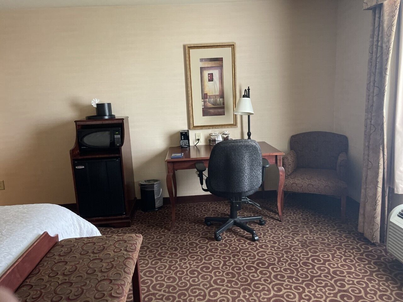 Een hotelkamer met een bed, een bureau met een computer, een stoel, een magnetron en een kleine koelkast.