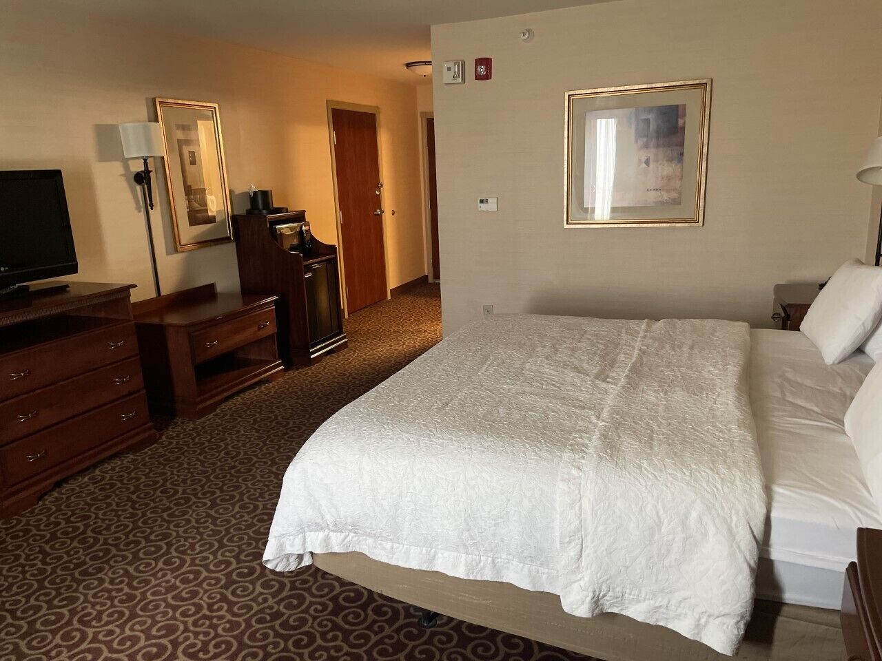 Een hotelkamer met een groot bed, een dressoir, een televisie en een spiegel.