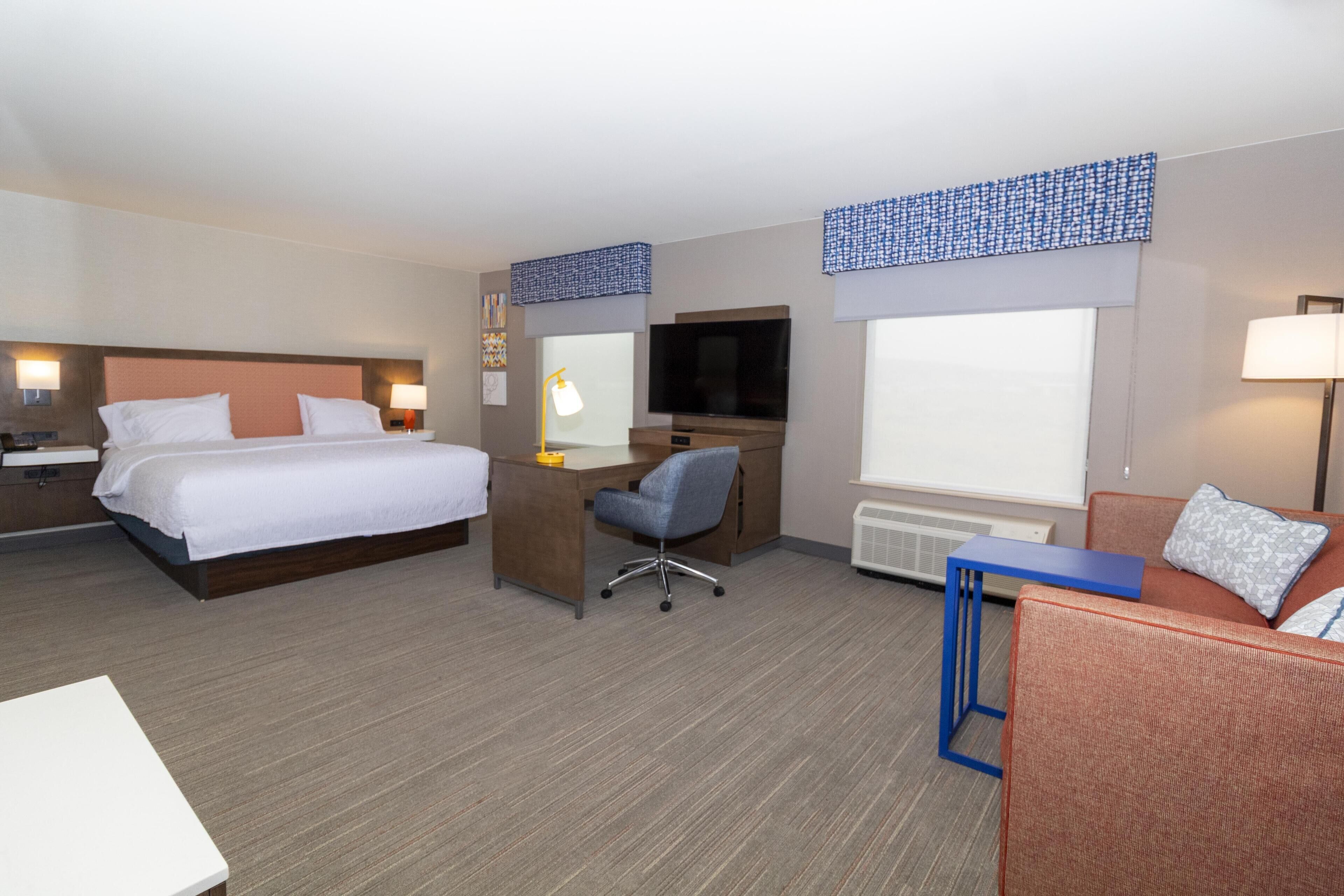 Habitación de hotel con cama, escritorio, silla, televisión y sofá.